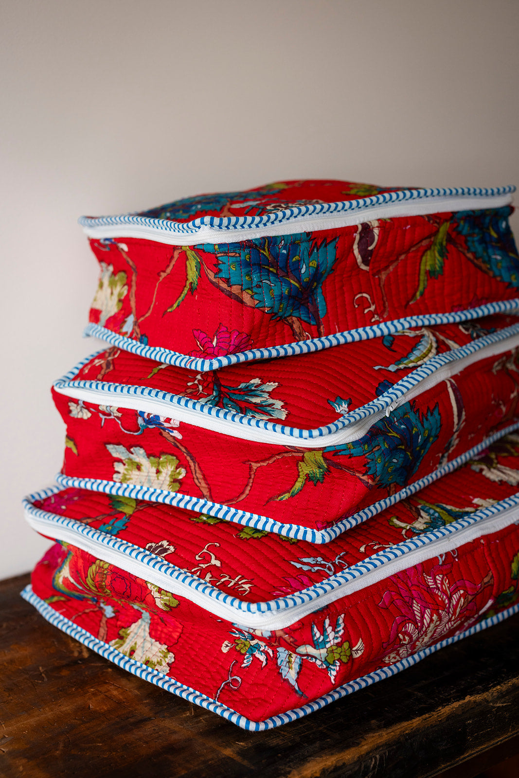 Stack of red fabric containers with floral patterns on a wooden surface