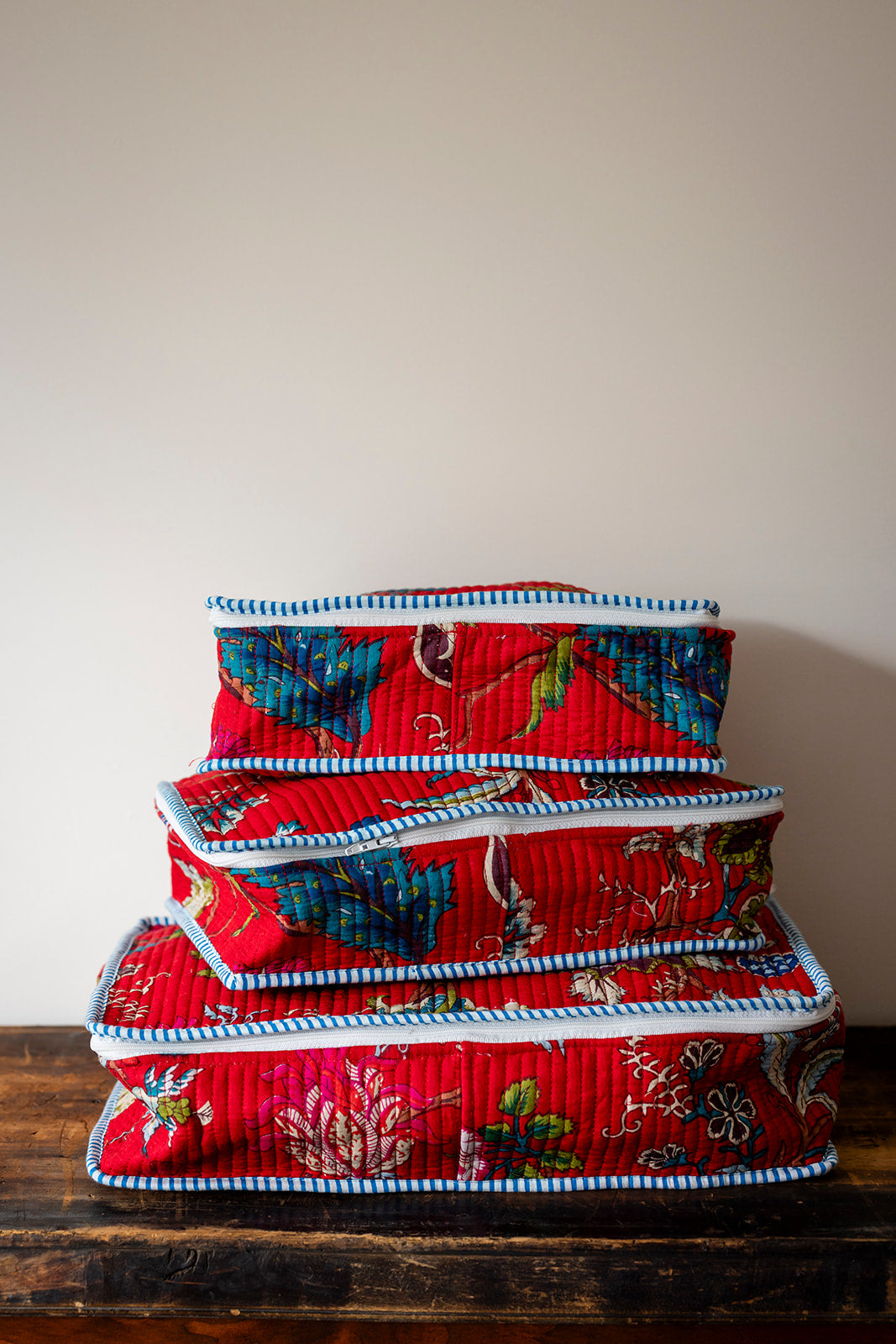 Stack of red fabric storage boxes with floral patterns on a wooden surface.