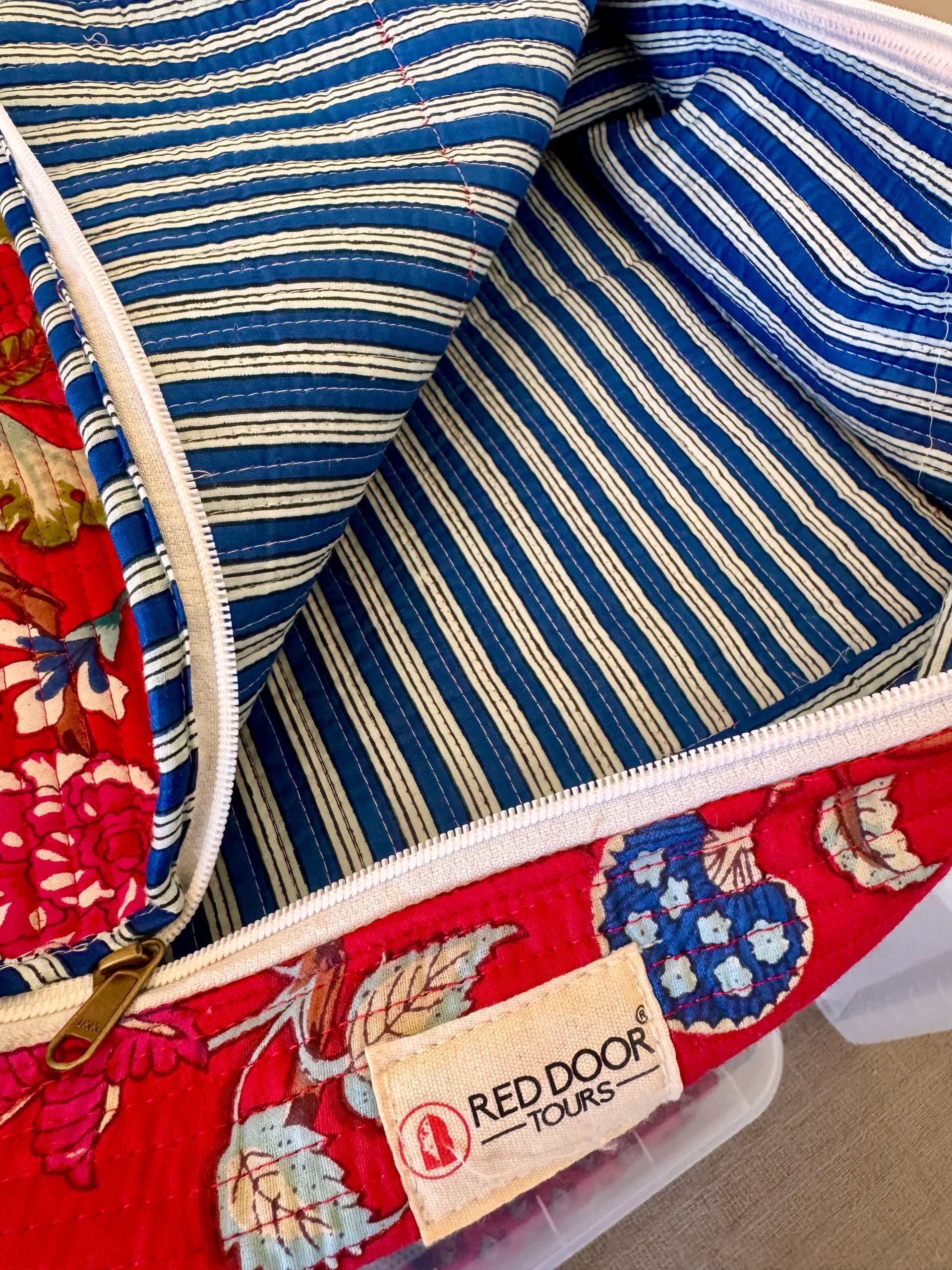 Close-up of a red door bag with floral pattern and striped interior, featuring a Red Door Tours label.