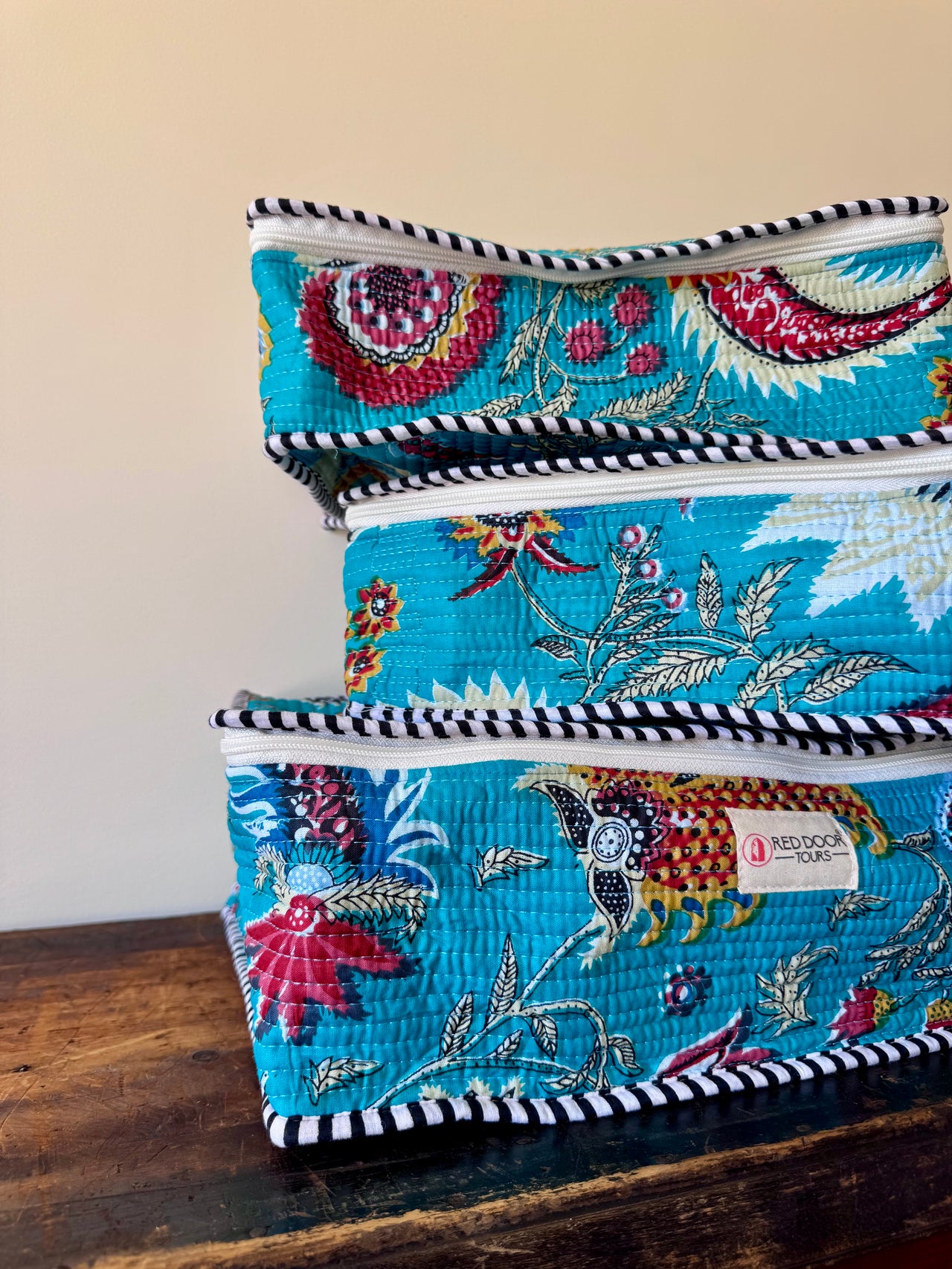 Stack of embroidered fabric bags on a wooden surface with a beige background