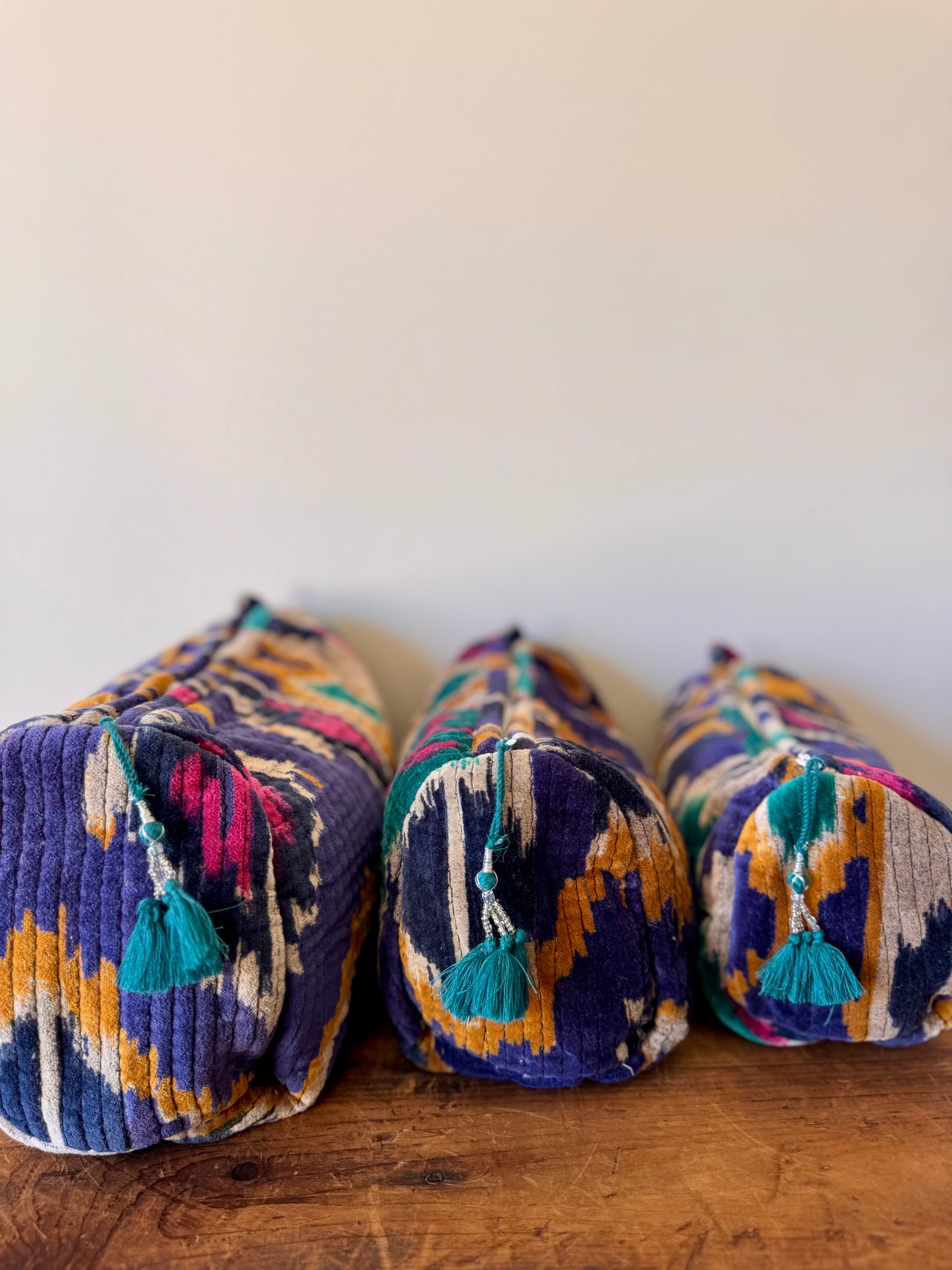 Three colorful cylindrical pillows with tassels on a wooden surface and white background