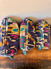 Three colorful patterned bags stacked on a wooden surface with a beige wall in the background.