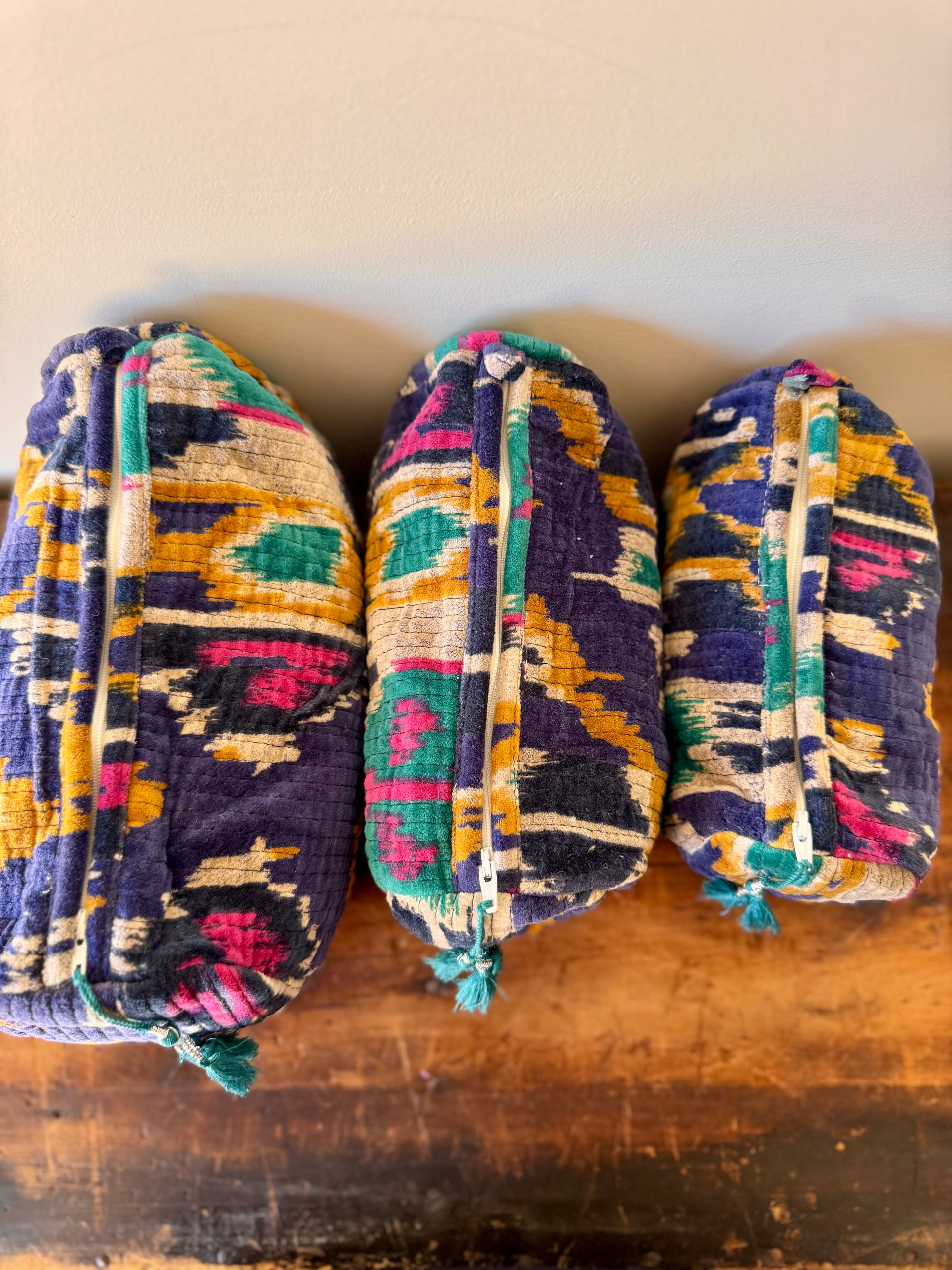 Three colorful patterned bags stacked on a wooden surface with a beige wall in the background.