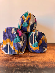Three colorful fabric bags with tassels stacked on a wooden surface.